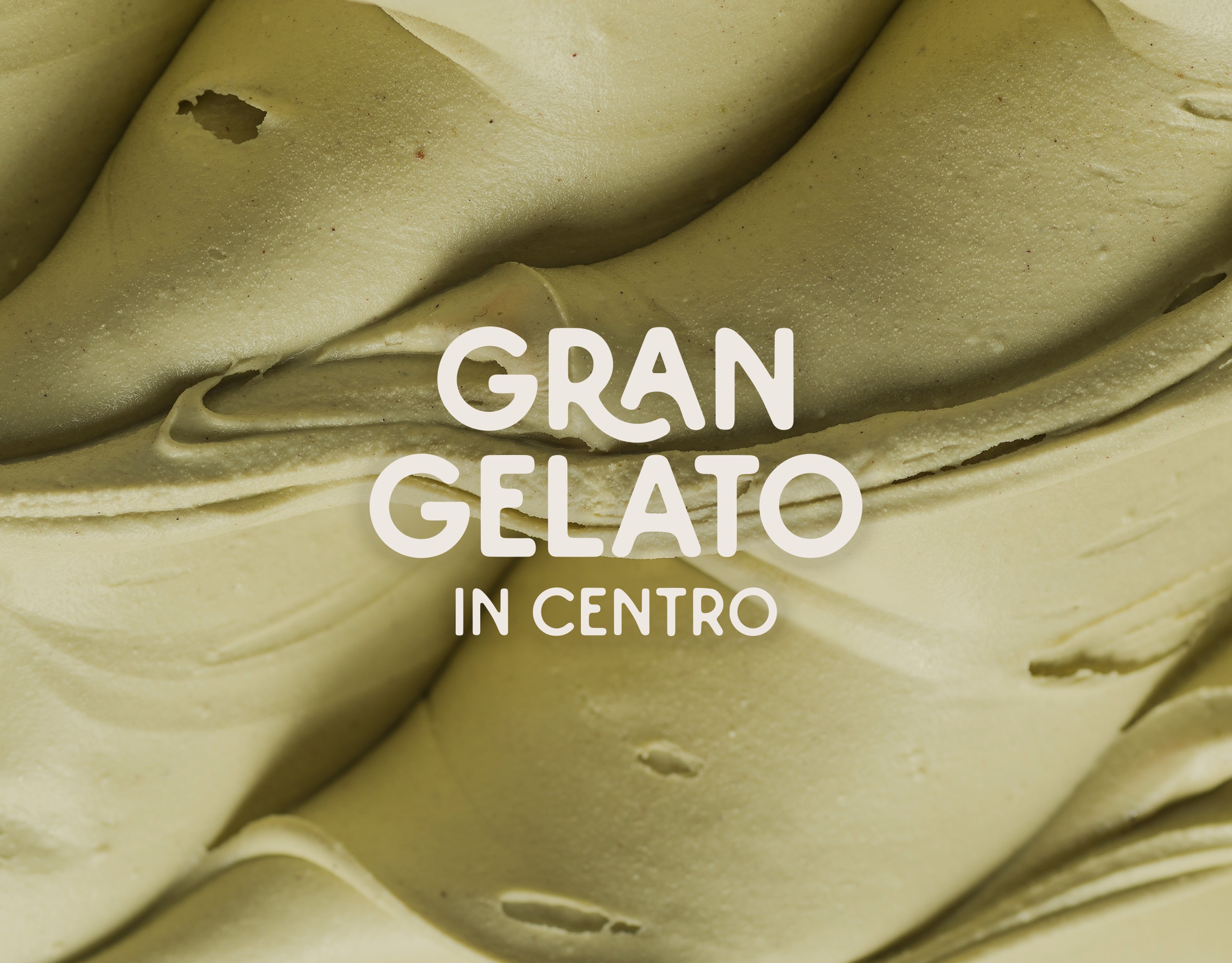 Primo piano di un gelato verde dalla consistenza cremosa e vellutata, con la scritta “GRAN GELATO IN CENTRO” in grassetto bianco sovrapposta alla superficie.